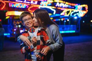A handsome boy together with his mother came to the amusement park to have fun and ride on the carousels and swings photo