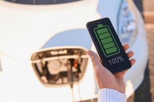 Smartphone app shows charging status of the electric car battery. Electro transport concept photo