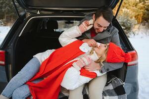 Smiling together. Nice couple have weekend at countryside at winter time. Sitting on the rear part of modern car. photo