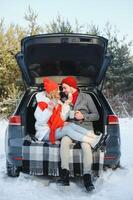 Smiling together. Nice couple have weekend at countryside at winter time. Sitting on the rear part of modern car. photo