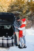 Smiling together. Nice couple have weekend at countryside at winter time. Sitting on the rear part of modern car. photo