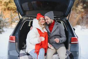 Smiling together. Nice couple have weekend at countryside at winter time. Sitting on the rear part of modern car. photo