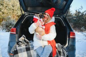 Woman resting in the winter forest sitting in the open trunk of a car with a dog. photo