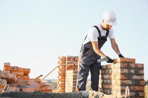 Construction worker man in work clothes and a construction helmet. Portrait of positive male builder in hardhat working at construction site photo