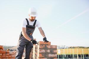 Construction worker man in work clothes and a construction helmet. Portrait of positive male builder in hardhat working at construction site photo