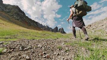 Back view Solo Hiker Walks in the wild with varied terrain while carrying a backpack and trekking poles. A man walks in the middle of mountains alone through rugged isolated landscape video