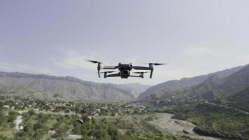 Quadcopter hanging in the air above green valley and growing trees. Action. Drone with spinning blades above mountains on cloudy sky backgrounds. photo
