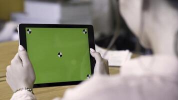 Rear view of a brunette woman using tablet with green screen, modern technologies concept. Stock footage. Female holding ipad with chromakey and reading something. photo