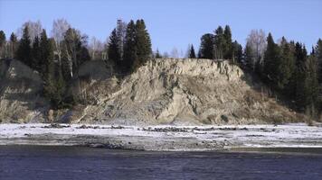 Natural landscape with a river in early winter and a hilly shore covered by trees. Clip. Stone cliff with forest and cold river. photo