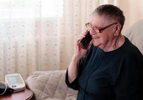 Retired senior engages in a phone conversation while a medical device for monitoring blood pressure sits nearby, demonstrating the integration of technology into daily life photo