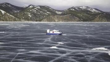 Hovercraft rides on lake Baikal. Clip. Aerial view of air cushion vehicle gliding on beautiful frozen lake with snow covered, forested mountains and cloudy sky on the background. photo