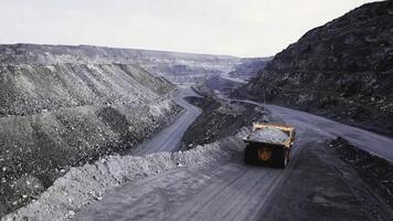 Dump truck is at quarry. Top view of driving orange dump truck with rubble on road open pit. Heavy transport in mining industry photo