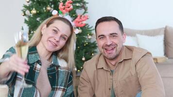 A married couple waves their hands, greets and communicates with relatives or subscribers via conference or online broadcast. Drink champagne or sparkling wine. New Year and Christmas. video