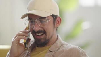 Talking in a phone call sitting on sofa at home, laughing and smiling happy man. video