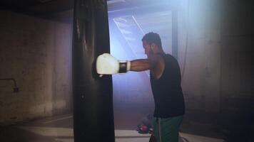 Professional boxer training with a boxing bag in dark gym in slow motion. Indoors exercise. video