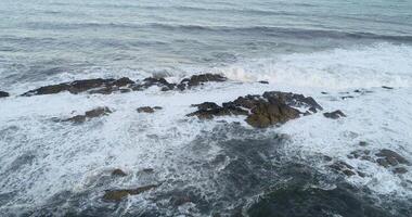 drone aerial view of the waves breaking on the rocks off the coast on a cloudy day, drone footage video