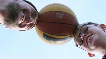 Family on basketball court in good mood having fun holding ball with head. Father and son pushing basketball with head in different directions. Fatherhood concept. video
