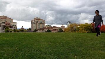a woman walking on the grass field in front of building and autumn trees video