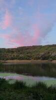 Pink clouds and a serene river reflecting the colors of twilight, surrounded by a lush landscape. video