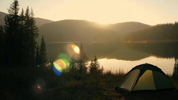 A serene scene of a tent by a calm lake, illuminated by the warm light of the setting sun. video