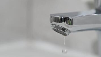 Drop of water drips from the tap. Beautiful fresh and clean water flowing from a tap. Close-up front view slow motion broken chrome faucet in the bathroom. Everyday problems, wasting water and energy video