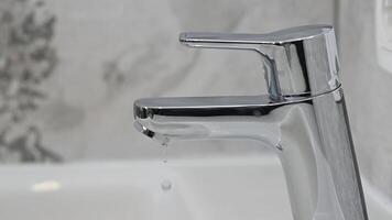 Drop of water drips from the mixer tap. Beautiful fresh and clean water flowing from a tap. Close-up front view broken chrome faucet in kitchen. Everyday problems, wasting water and energy video