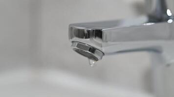 Drop of water drips from the tap. Beautiful fresh and clean water flowing from a tap. Close-up front view broken chrome faucet in kitchen. Everyday problems, wasting water and energy video