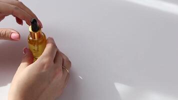 hands above a white table, open a small bottle of golden oil with a pipette lid. video