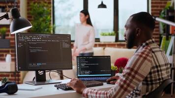 Male coder works from home typing code on a laptop in a modern living room. African american IT engineer using programming language and cloud computing for software development. Camera B. video