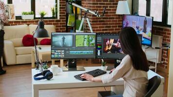 Asian woman editing a music in her living room studio, multitasking between timeline editing and color grading. Professional workspace features tech tools for multimedia creation. Camera A. video