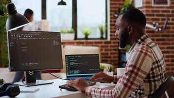 jovem homem visto programação Programas código em dele computador portátil dentro uma lustroso casa escritório. área de trabalho com dual monitores ajuda com Programas Engenharia, rede desenvolvimento e codificação produtividade. Câmera b. video