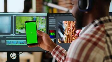 afrikanisch amerikanisch Mann bearbeitet ein Musik- beim seine Zuhause Büro Nächster zu Kopieren Raum Bildschirm, mit Bearbeitung Software und Dual überwacht. lösen Produktion und freiberuflich tätig Aufgaben. Kamera b. video