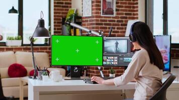 Female editor working on a creative project shoot, using chroma key copy space screen next to color grading software. Home workspace highlights productivity. Camera B. video