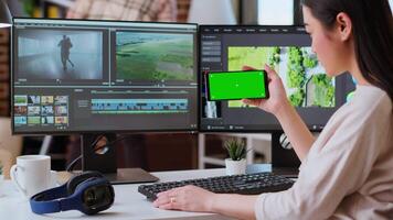 Female editor working on a creative project shoot, using chroma key copy space screen next to color grading software. Home workspace highlights productivity. Camera B. video