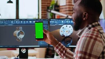 Software developer creates a gear prototype on dual monitors next to chroma key display, home office remote work. Expert does 3D modeling for innovation in the industrial design industry. Camera B. video