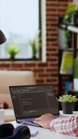Vertical African american software developer works on programming code on a laptop in remote workspace. Productive IT engineer working on coding, software design and internet security innovation. Camera B. video