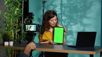 Woman holding green screen tablet, talking about specifications, filming with professional camera. Internet show host presenting chroma key device features, recording with filming gear, camera A video