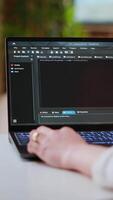 Vertical Asian female programmer works on coding software in a home office setup, typing code on a laptop. IT expert uses digital tools for multitasking, software development and app development. Camera B. video