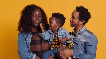 African american mom and dad teaching their son how to sing in studio, learning to perform songs on microphone from a young age. Adorable little boy singing a new melody. Camera A. video