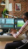Vertical African american man editor working in production industry, does color grading and editing a film project on dual monitors. Showing the creative process with tech tools. Camera A. video