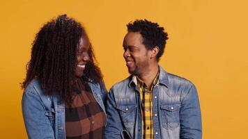 African american life partners smiling and looking at each other, flirting and showing affection against yellow background. Joyful husband and wife embracing beloved soulmates. Camera A. video
