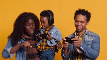 Joyful optimistic dad playing online games with his boy using controller, parents enjoying leisure time with their small child. African american happy family play together in studio. Camera A. video