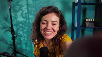 Cheerful influencer in home studio using handheld camera to record live broadcast, greeting subscribers. POV shot of happy internet show host doing house tour with viewers video
