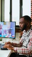 Vertical Male coder works from home typing code on a laptop in a modern living room. African american IT engineer using programming language and cloud computing for software development. Camera A. video