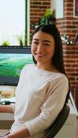 Vertical Asian woman editor working with dual monitors in living room, editing footage and color grading in a modern office setup. Perfect for post production and media creation. Camera A. video