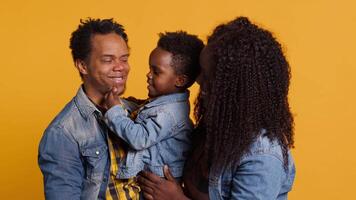 Portrait of african american family with a small boy posing in studio, showing affection and love towards each other and feeling happy. Grateful husband and wife holding their toddler. Camera A. video