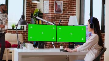 Asian woman solving her freelance tasks with isolated copy space on screen, using headphones while she does research for a project at home office. Remote working and multitasking. Camera B. video