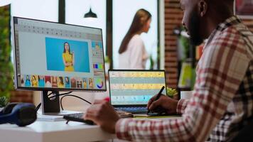 Male african american designer works with photo editing software in his creative workspace at home. Using dual monitors to ensure productivity and innovation in the graphic design world. Camera B. video