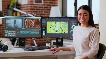 Asian woman editor working with dual monitors in living room, editing footage and color grading in a modern office setup. Perfect for post production and media creation. Camera B. video