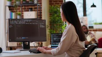 Asian female developer coding cloud computing applications on pc in a modern tech workspace. Woman IT specialist focuses on the software development process for productivity and innovation. Camera B. video